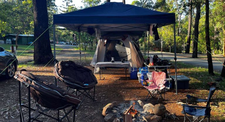 Family glamping setup at Thunderbird Park Tamborine Mountain Glades showing large tent, gazebo, dining area, and fire pit in a spacious unpowered campsite surrounded by rainforest trees