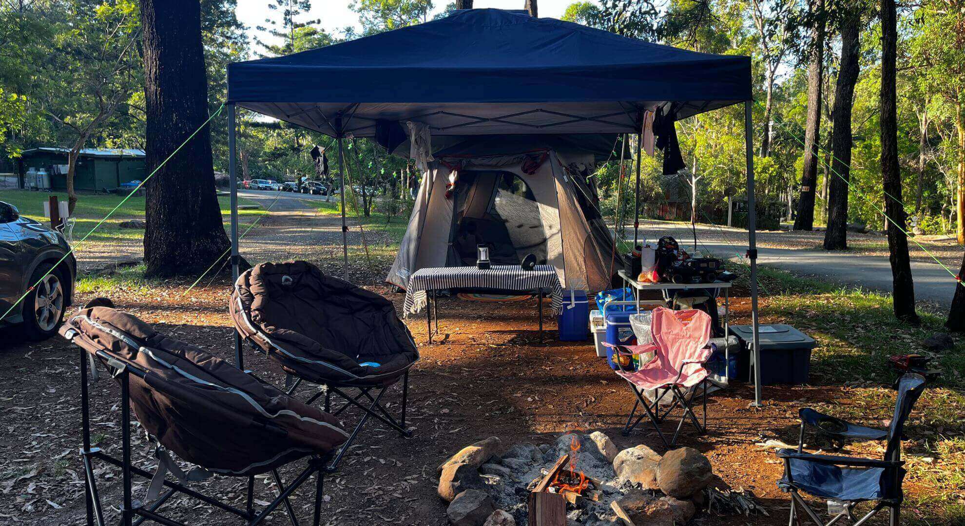 Family glamping setup at Thunderbird Park Tamborine Mountain Glades showing large tent, gazebo, dining area, and fire pit in a spacious unpowered campsite surrounded by rainforest trees